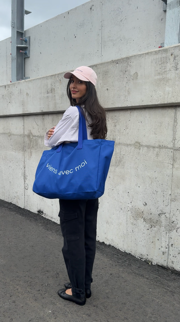 Oversized canvas tote bag by viens avec moi in royal blue, with white font print on the bag that reads viens avec moi in the shape of a smile.