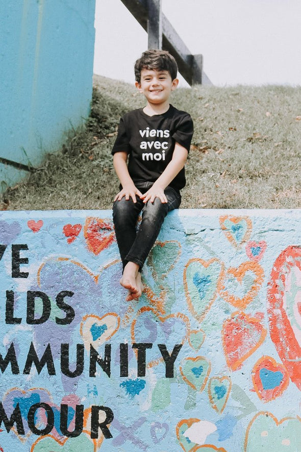 The Viens Avec Moi Kids Tee in Black. The 100% cotton tee with a white screen print is comfortable and super cute.
