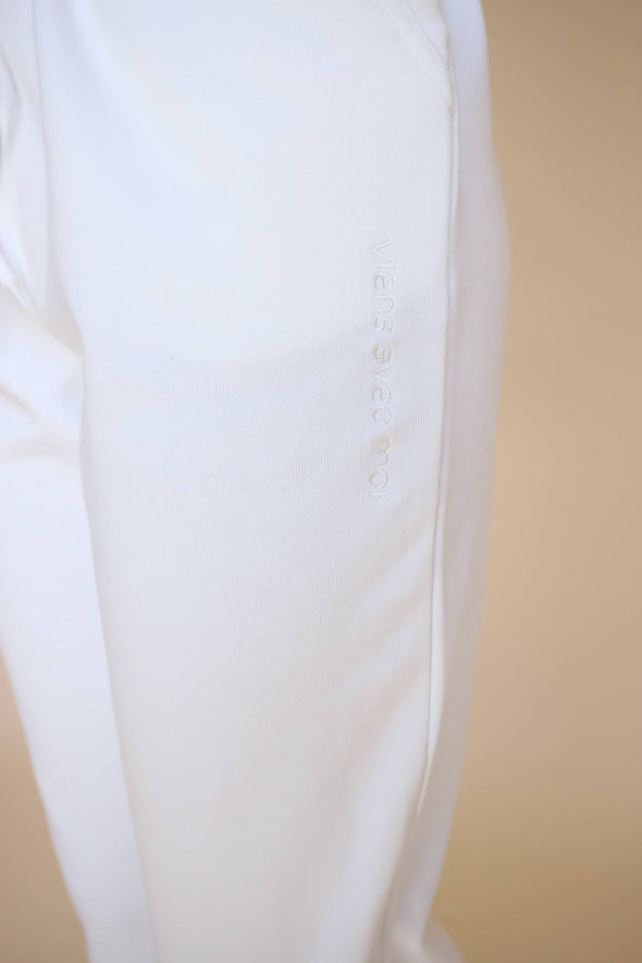 Closeup of the embroidered 'viens avec moi' detail on the side seam of the lightweight white jogger pants.