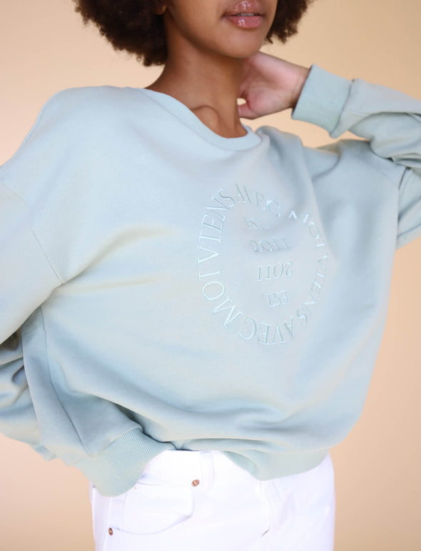 The Lakeside Crew Sweater in Seafoam is made of eco=conscious fabrics and features a cropped cut, dropped shoulder detail and embroidered logo design on front.