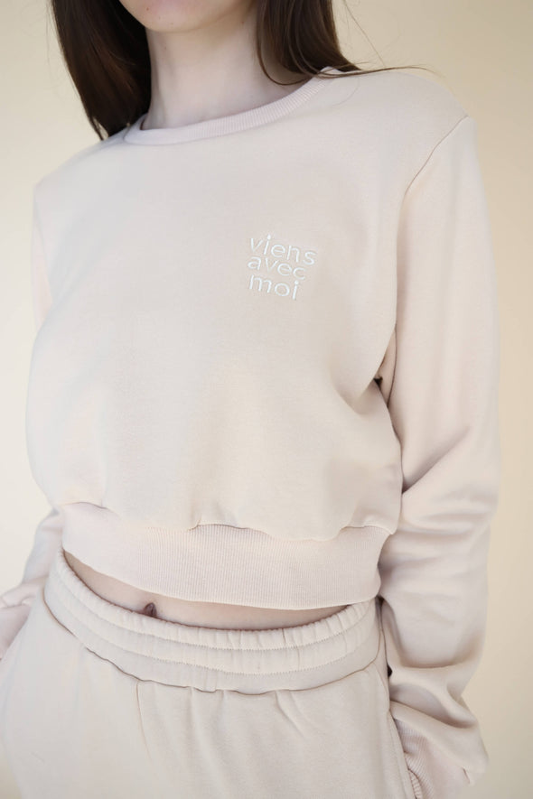 Closeup of the Viens Avec Moi logo chest pocket design and the cropped length on the nude coloured, cropped sweater.