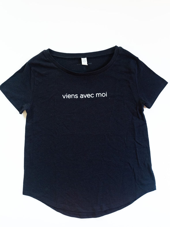 The Viens Avec Moi Black Tee is a relaxed fit tshirt with white front viens avec moi logo, wide neckline and scooped, high-low hemline.